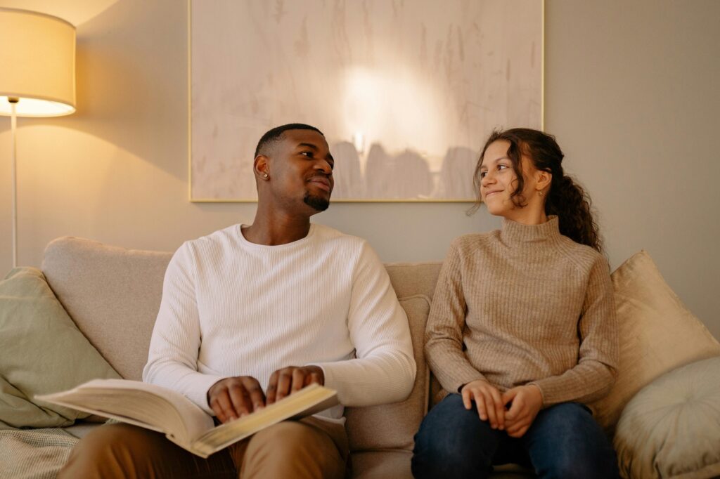 A man and girl enjoying quality time reading a Braille book together on a cozy sofa.